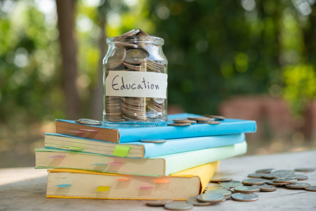 Student Loan Repayments and Education Finance Education savings jar filled with coins on a stack of books, representing student loan repayments and education costs.
